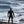Der Maverick von hinten im Neoprenanzug mit Haube und Surfboard vor dem wilden winterlichen Ozean – HOUSE OF 3 II · 02 UNBROKEN